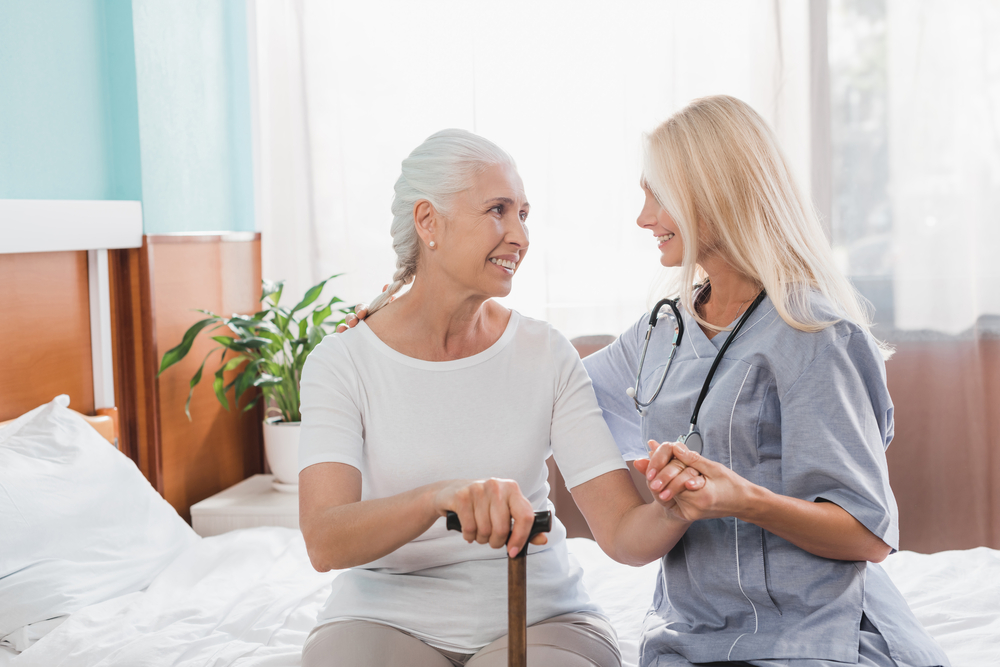 Health care professional helps a senior woman in short-term rehabilitation to get out of bed